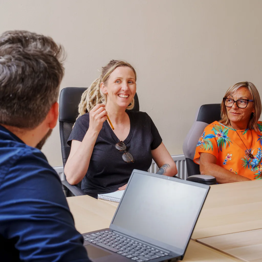 A smiling woman wearing a black shirt sits at a meeting table, participating in a group discussion.