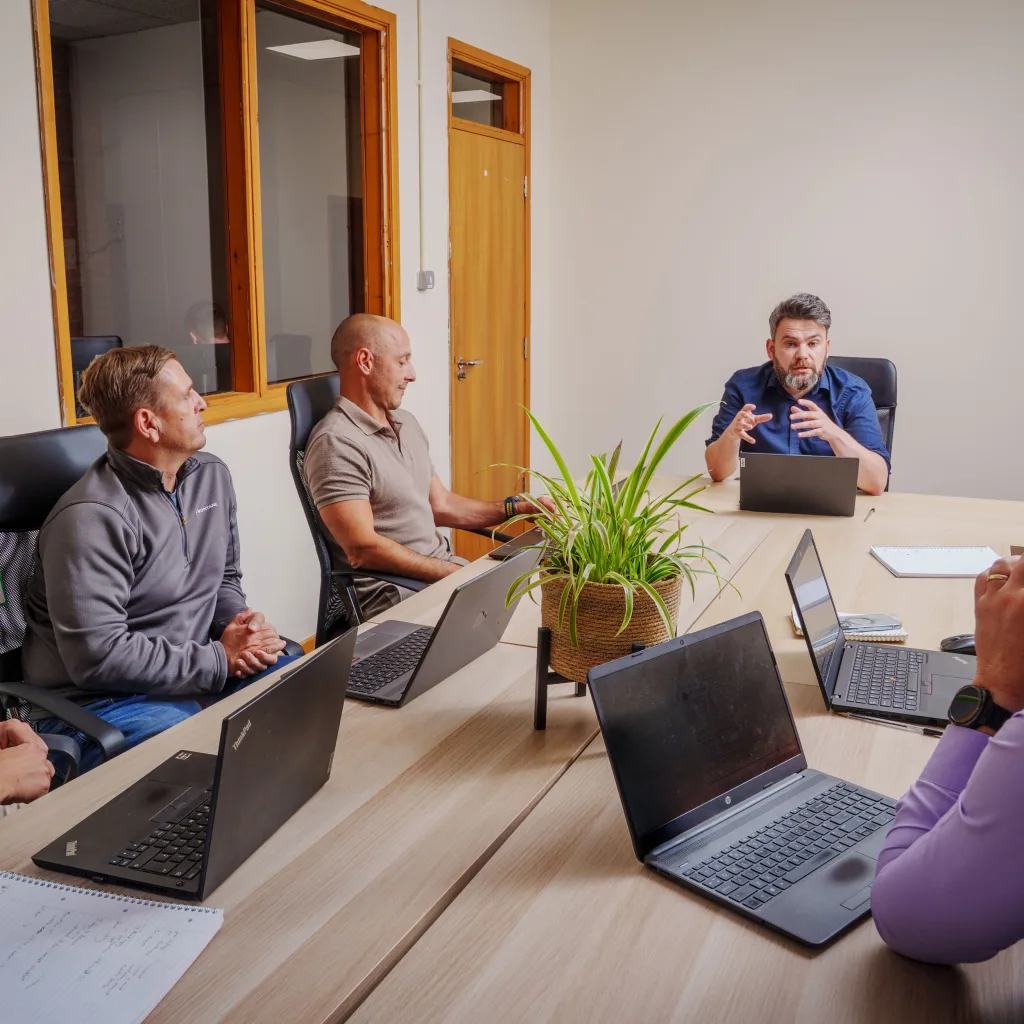 A team of people sitting around a table, each with laptops, engaged in a collaborative meeting.
